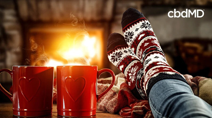 Two legs are propped up with christmas socks on the feet in front of a warm fire