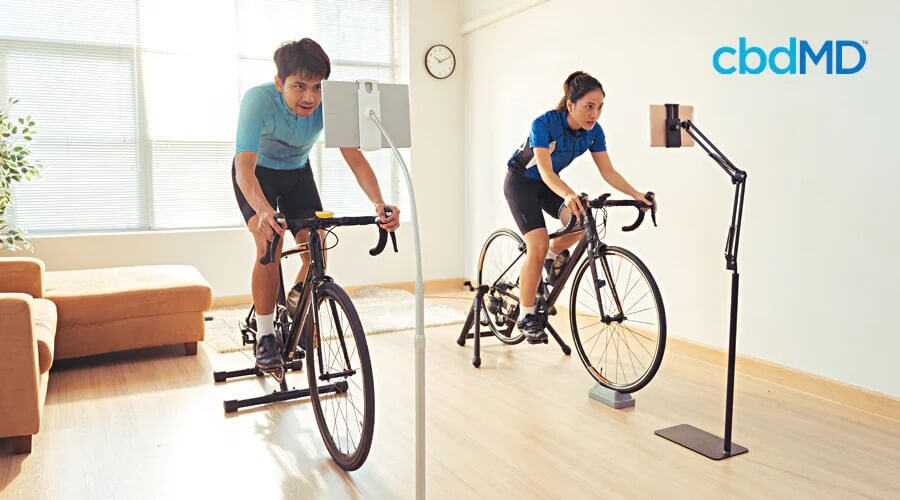 Two friends ride exercise bikes in their living room