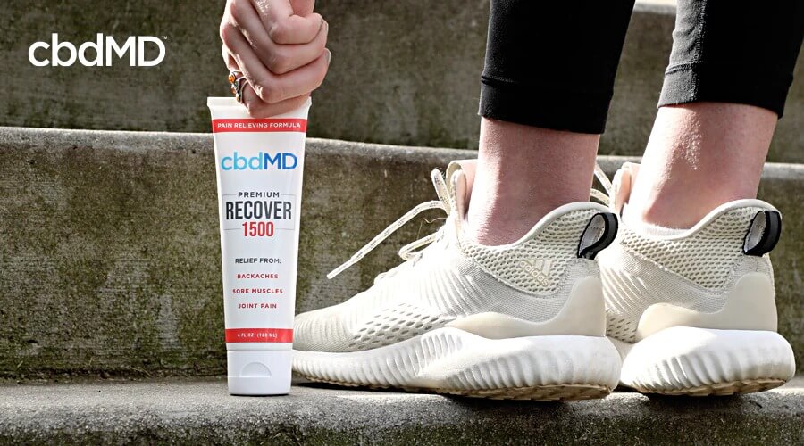 A tube of 1500 mg cbd recover from cbdmd sits on a stone step next to a person in running shoes