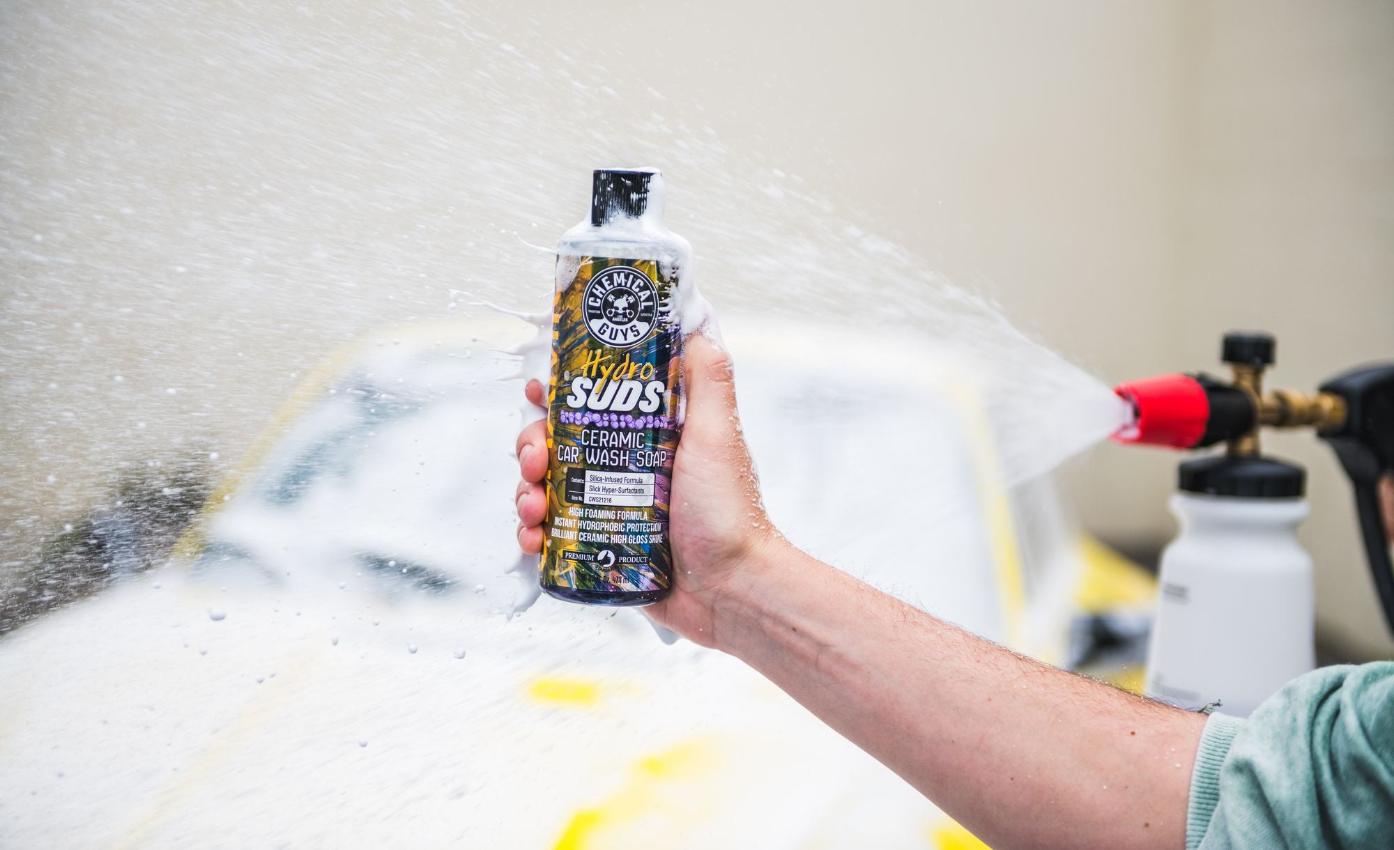 HydroSuds bottle in front of a car covered in sudsy car wash foam