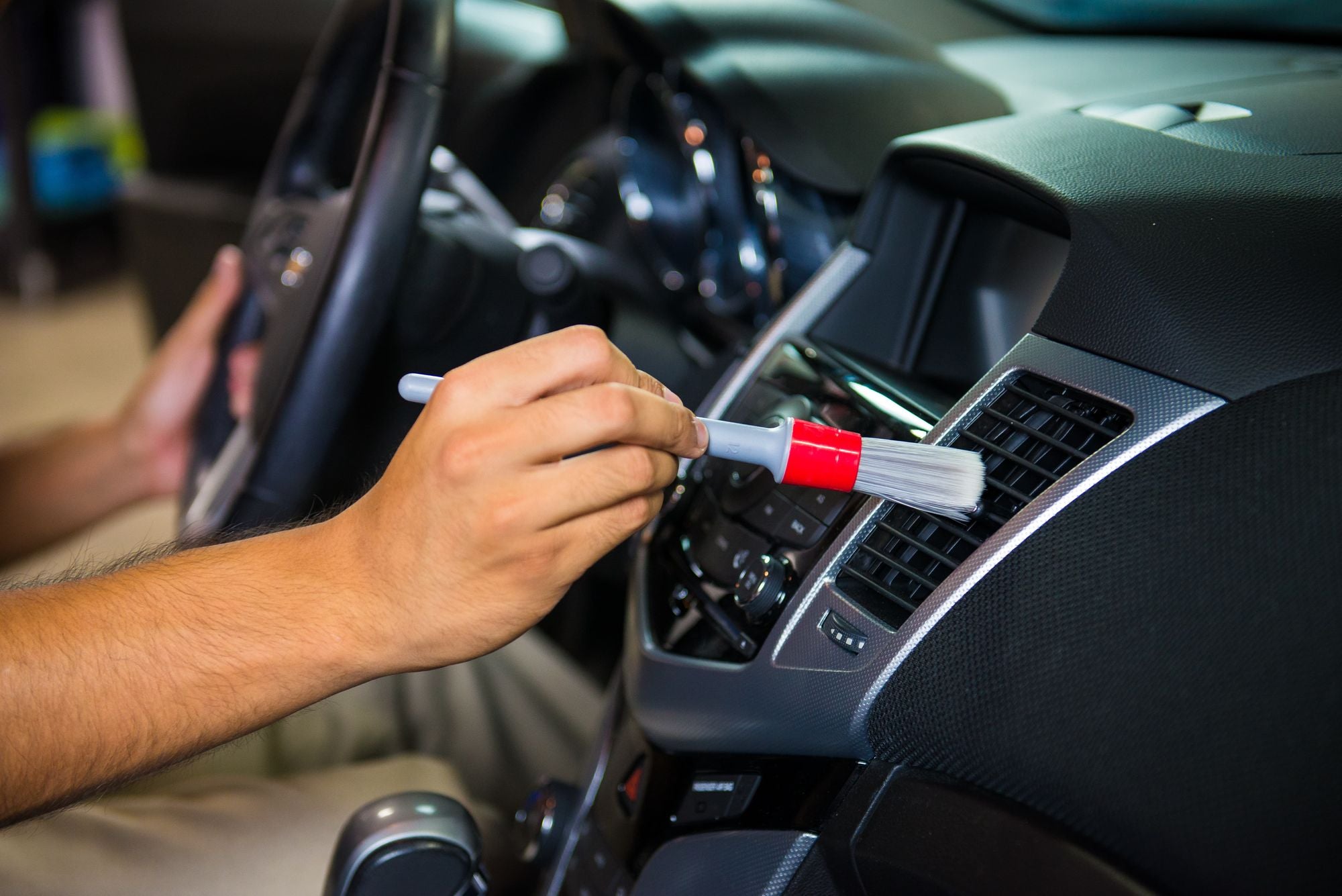 Cleaning a car dashboard A/C vent with one of the included All in the Details Interior Detailing Brushes