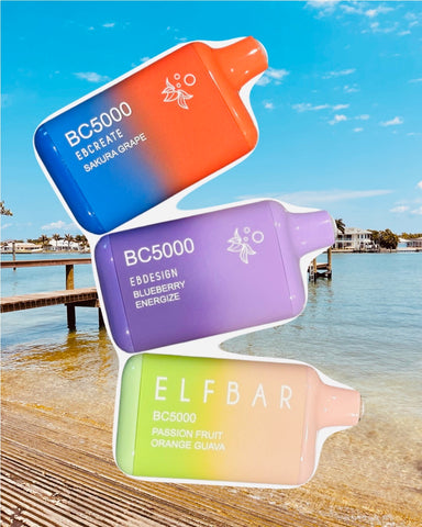 The image shows three oversized vape liquid bottles displayed against a coastal backdrop. The top bottle is red with the text "BC5000 EBCREATE SAKURA GRAPE," the middle one is purple and reads "BC5000 EBDESIGN BLUEBERRY ENERGIZE," and the bottom bottle is green and labeled "ELFBAR BC5000 PASSION FRUIT ORANGE GUAVA." The bottles are superimposed as if floating above a wooden dock leading to a calm sea under a blue sky. Each bottle features a minimalist bee icon near the neck. The setting suggests a serene, leisurely day by the water.