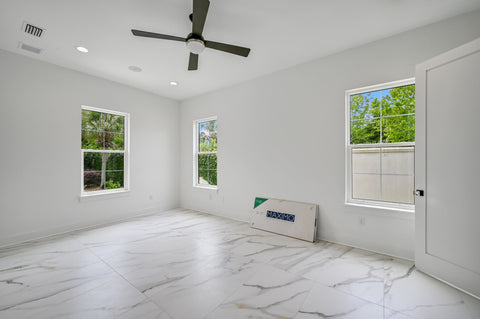 An unstaged, new construction primary bedroom with white marble tile and a black ceiling fan.
