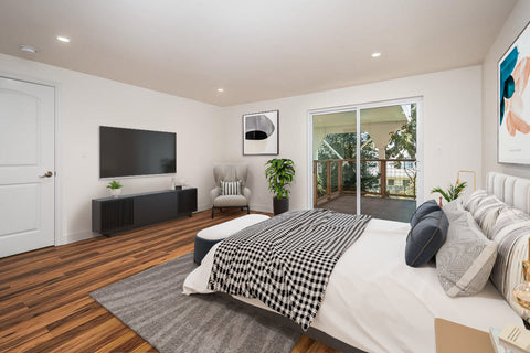 A Virtually staged primary bedroom, with black and white blankets, and a television along the left wall