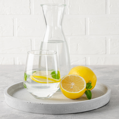 Circular tray sitting on a table. It is holding a pitcher of water, a glass and two lemons.