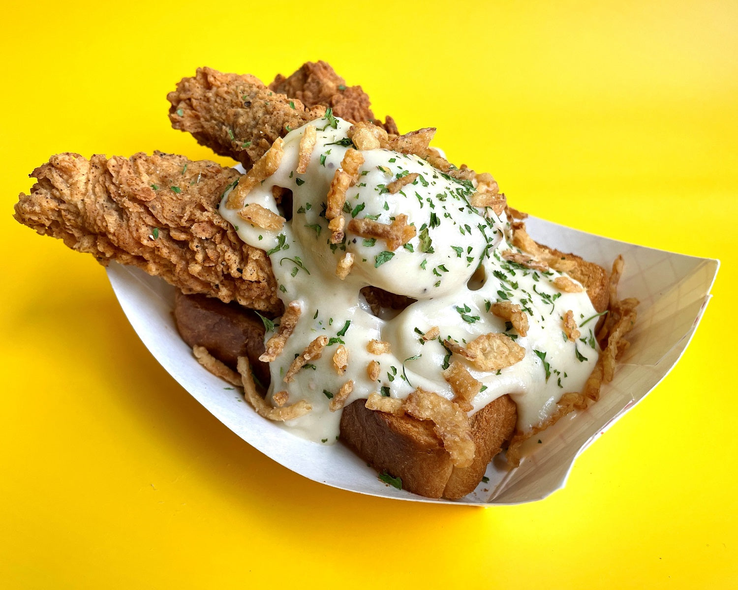paper boat with texas toast topped with vegan chicken fried steak tenders, sausage gravy, fried onions and parsley flakes for the minnesota state fair