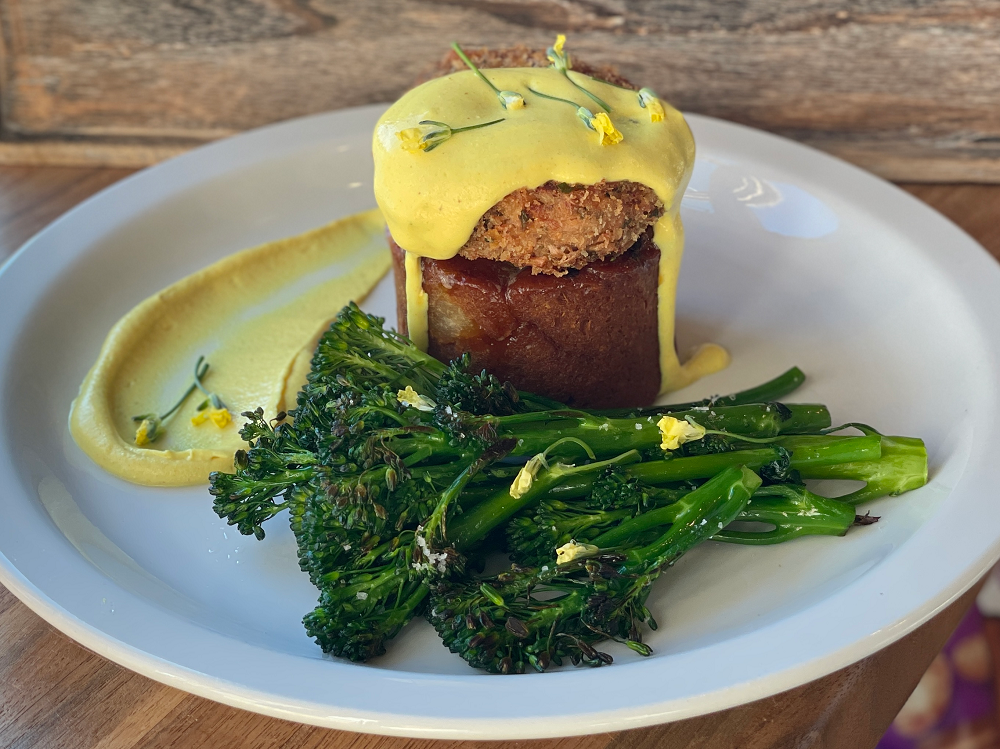 vegan filet mignon topped with a vegan crab cake and yellow sauce with a side of broccolini