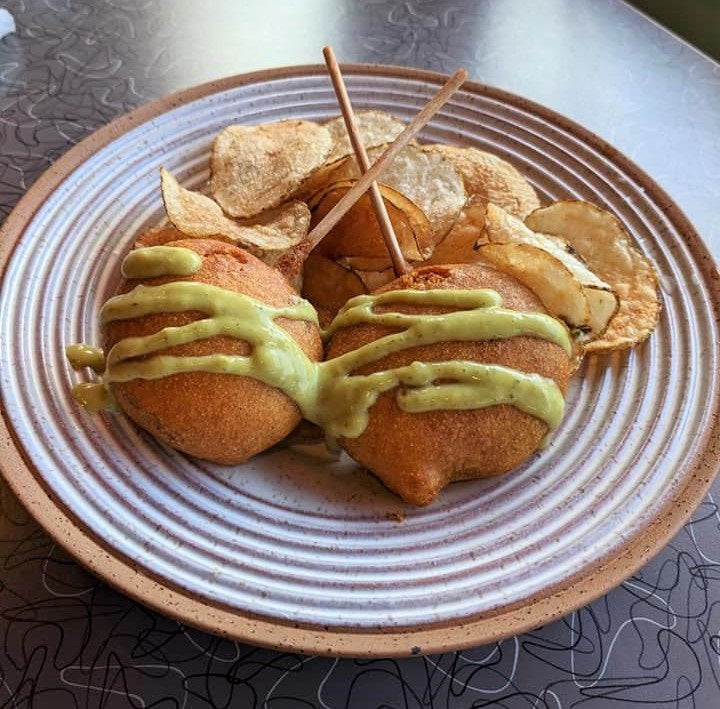 two corn dog pop drizzled with green sauce and a side of potato chips