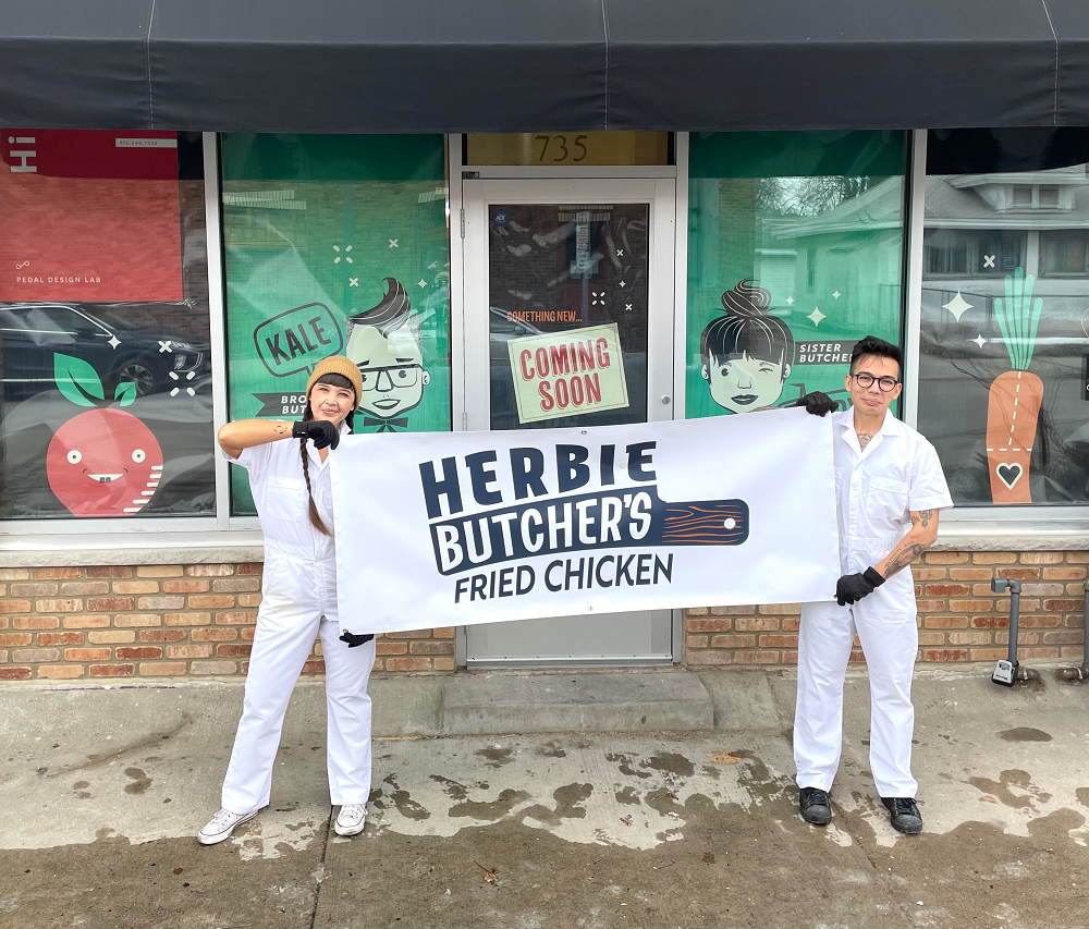 two people holding a sign for Herbie Butcher's Fried Chicken