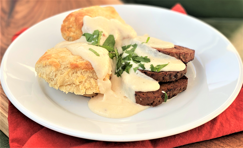 two biscuits with slices of vegan sausage topped with white gravy on a plate