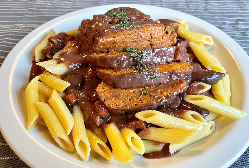 sliced vegan steak on a bed of penne pasta with red wine sauce