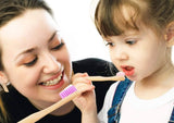 Woman teaching young girl how to brush teeth