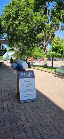 Outside of Makers Mercantile & Studio features a sign with blue, white, and gray balloons