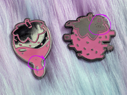 Photo of two B-Grade strawberry-themed enamel pins, circling the small visual defects that make them a B-Grade