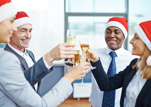 Four business colleagues stand in office during holiday season wearing Santa caps, toasting each other with champagne flutes.