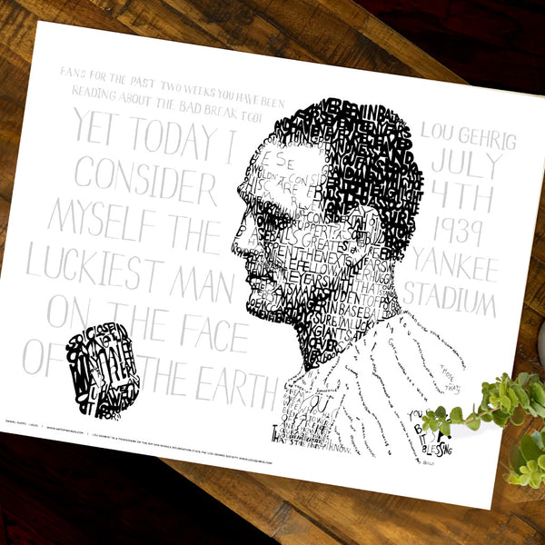 Unframed Lou Gehrig art print, a word art portrait of him giving his “Luckiest Man” speech, lies flat on wood table.
