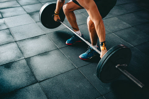 A lower body shot of a man in the middle of performing a deadlift at the gym.