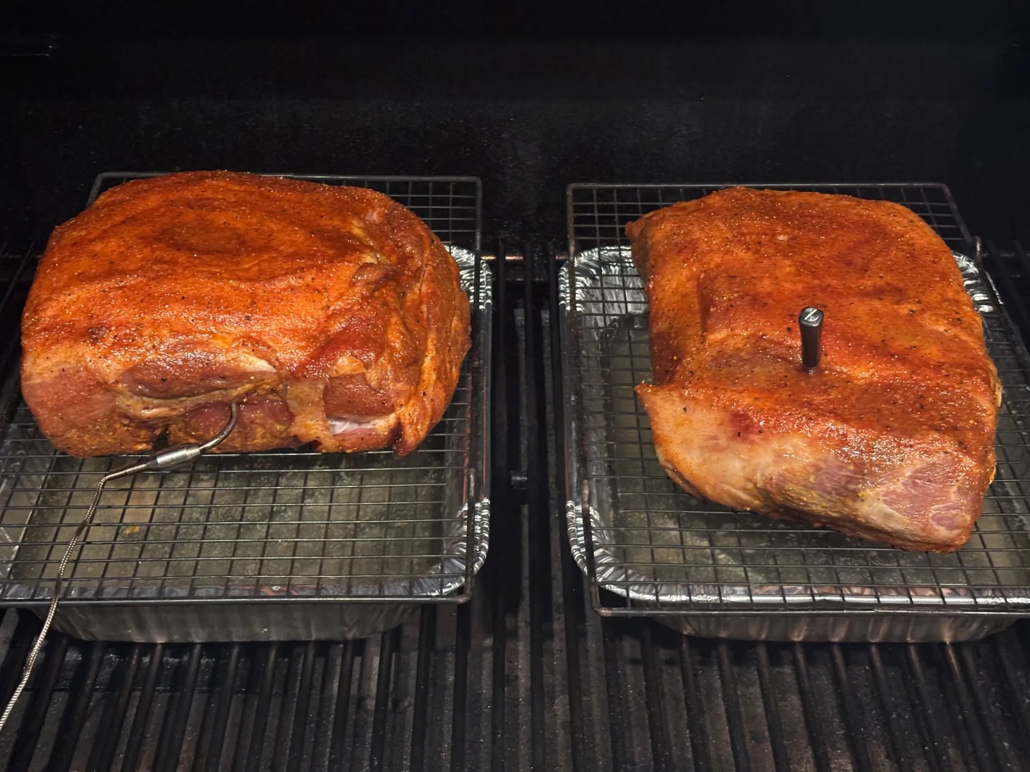 Pork butts on wire racks in the smoker with temperature probes inserted
