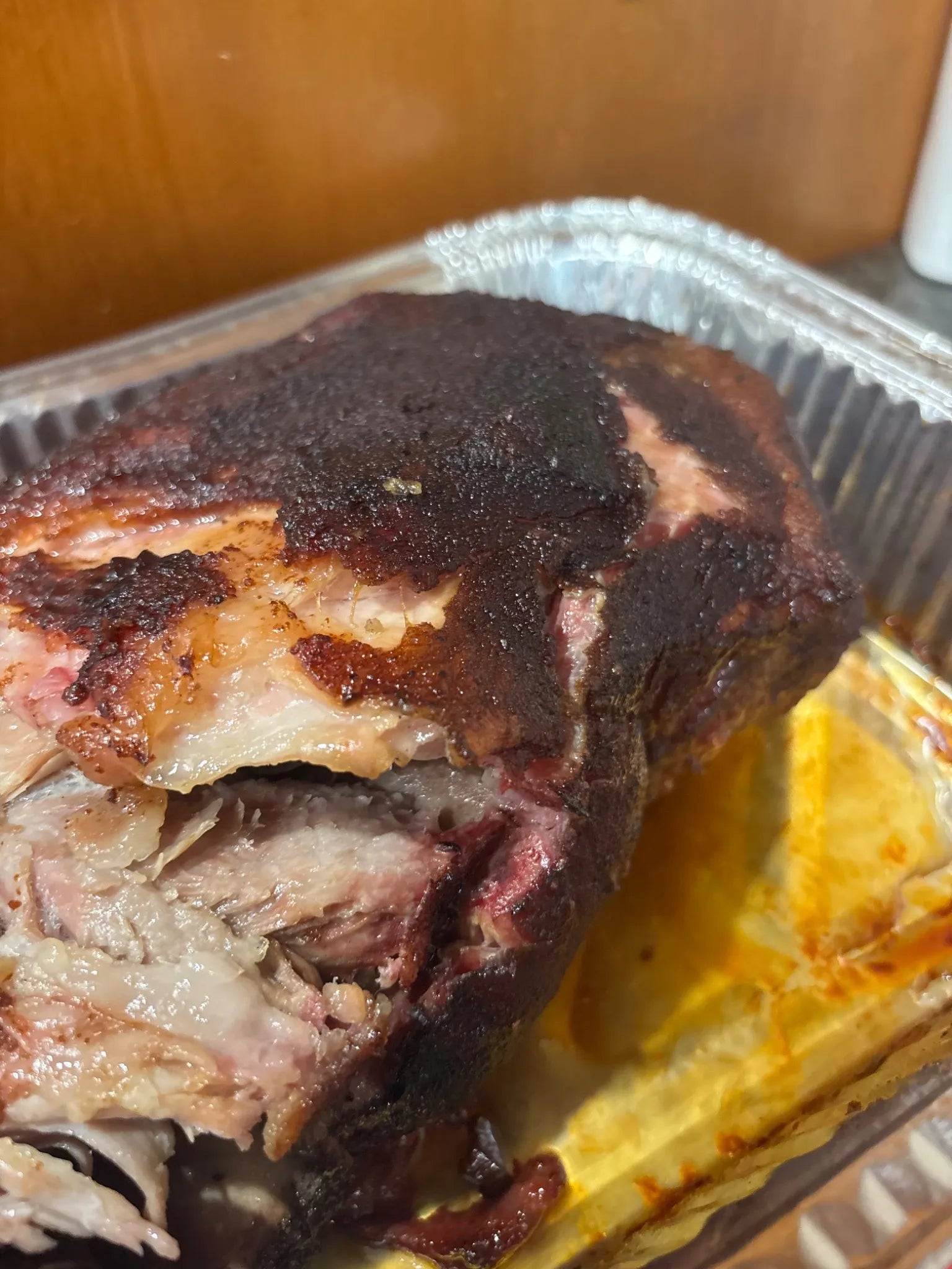Smoked pork butt resting in a foil tray with visible smoke ring and tender meat
