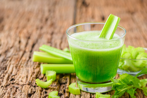 An image of fresh green celery juice in glass with celery on the side.