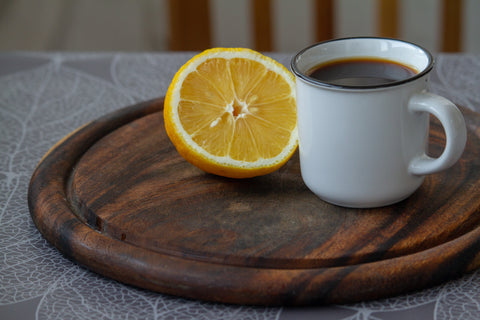 An image of a black cup of coffee with a half of a lemon on a table.
