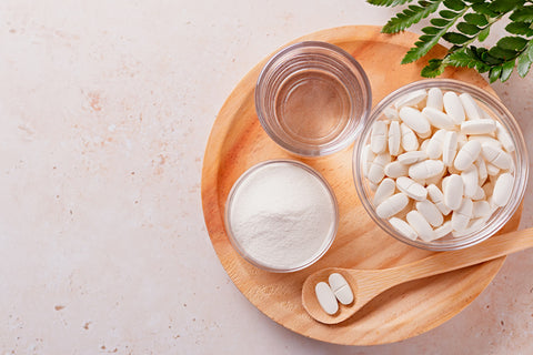 An image of Collagen powder, pills, wooden spoon, and glass of water on wooden tray,