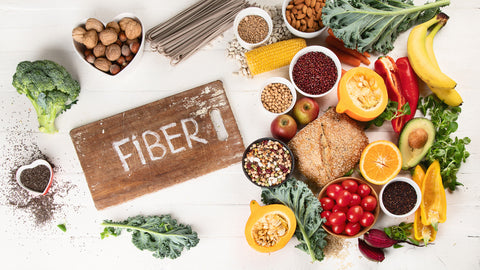 An image of assorted high-fiber foods, including walnuts, bananas, whole wheat bread, cherry tomatoes, and beans, with text that reads fiber. 