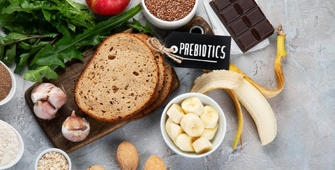An image of prebiotic foods, including flax seeds, dark chocolate, banana, whole wheat bread, almonds, garlic, oats, rice, and an apple with text that reads prebiotics.