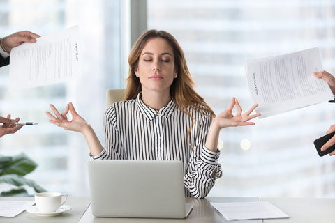 An image of a female executive meditating in a stressful office. 