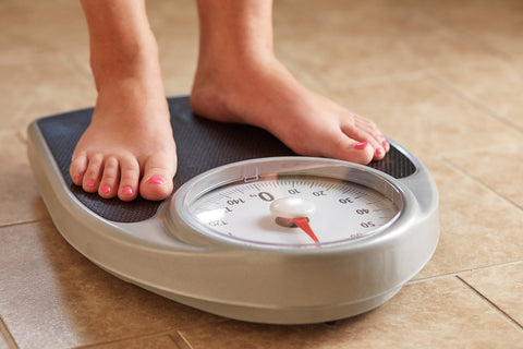 An image of female bare feet on a weight scale in the bathroom.