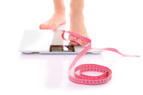 An image of female feet stepping onto a bathroom scales and a tape measure on a white background.