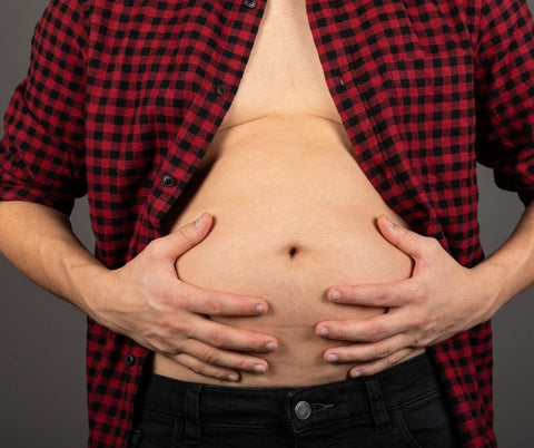 A cropped image of a man with an open shirt holding his bloated stomach.