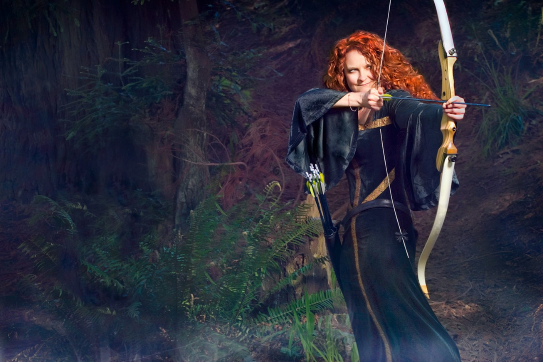 jessicurl founder, Jess McGuinty, dressed as Merida from Brave in a green dress and bow standing in a forest