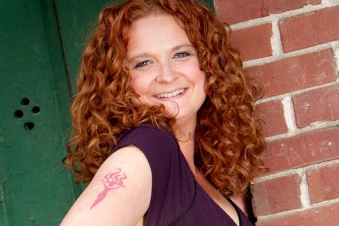 Jess smiling with her "full body logo lady" tattoo visible on her upper arm.