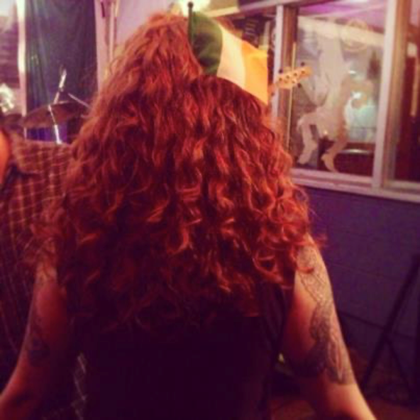back of red, curly haired woman's head with a small Irish flag in her hair