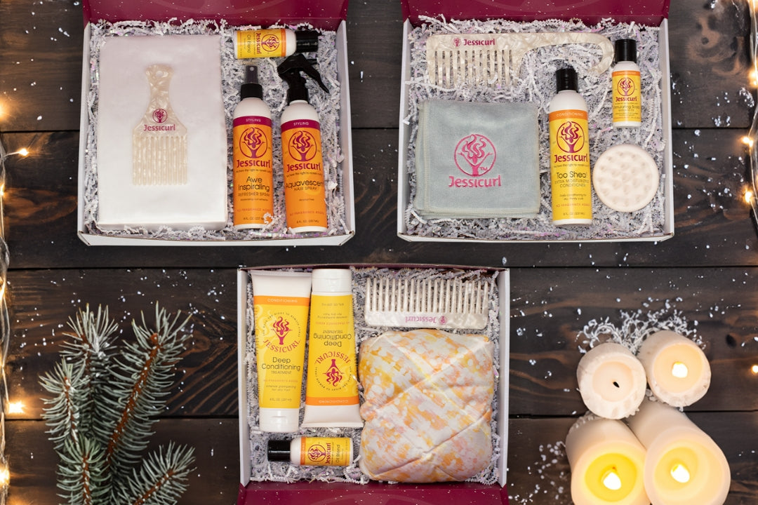 three holiday bundle boxes of products and accessories on a wooden table surrounded by foliage, lights, and candles