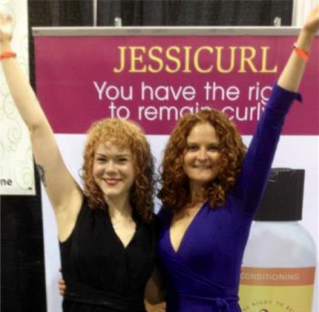 two curly haired woman with one arm around each other and the others raised up