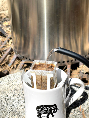 kettle pouring water into a travel pour over bag anchored to a mug with Lanna Coffee's elephant logo