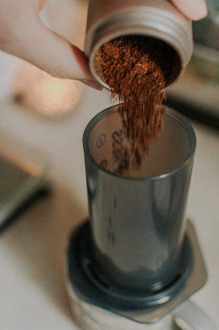 medium-fine coffee grounds being poured into AeroPress coffee maker