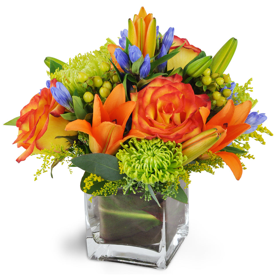 Autumnal Glory. Flower arrangement Includes seasonal roses, lilies, and more for a memorable autumn impression that is sure to brighten any day. In a clear square vase.