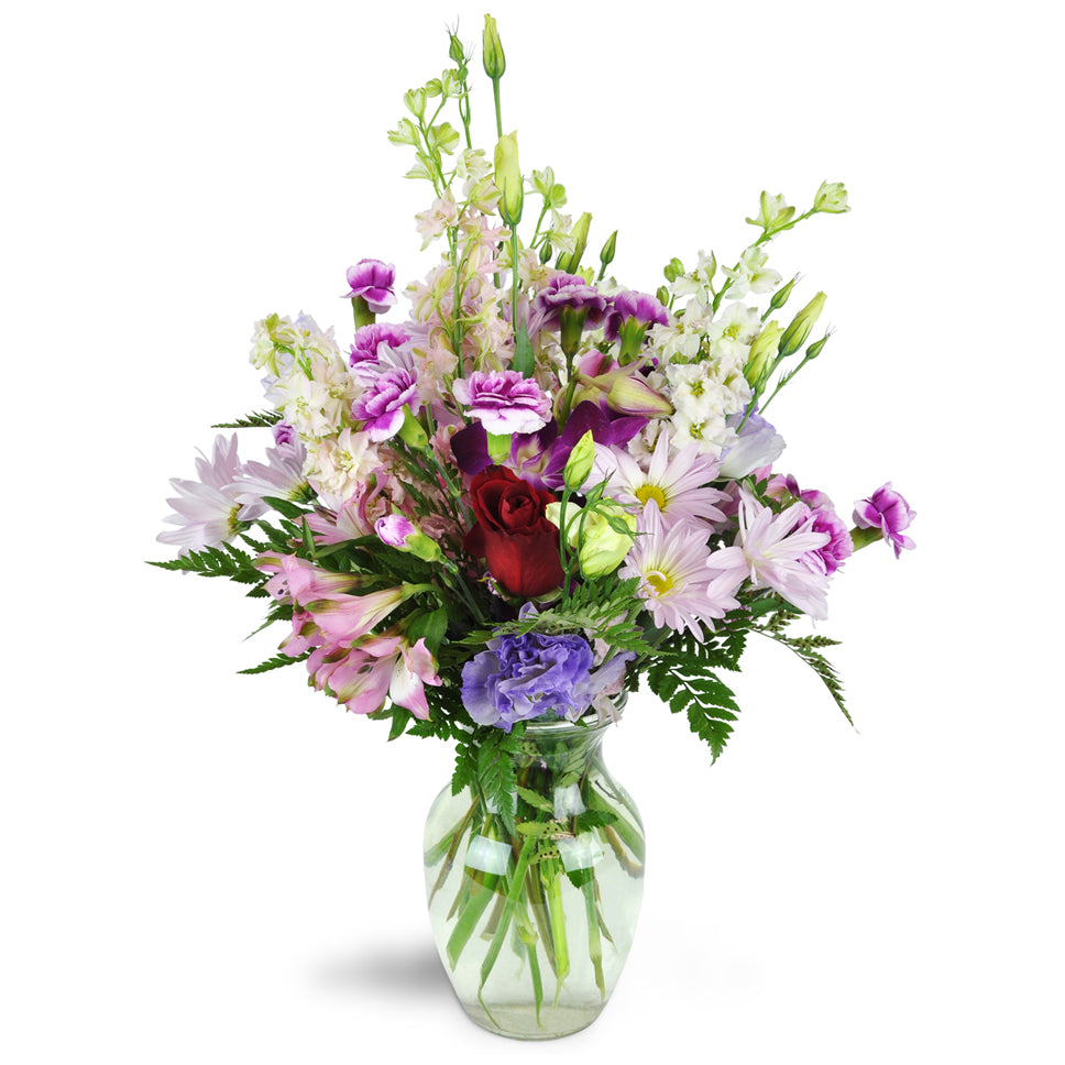 Morning in the Garden™. Roses, mini carnations, larkspur, Peruvian lilies, and a stem of Dendrobium orchids are elegantly arrranged in a glass vase.