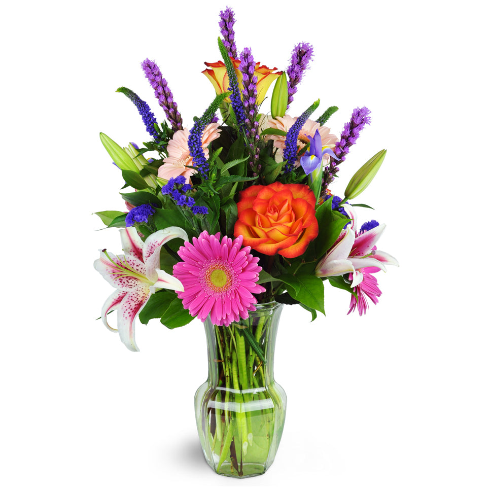 Jazzy Splash™. Gerbera daisies, roses, lilies, and more are arranged in a glass vase.