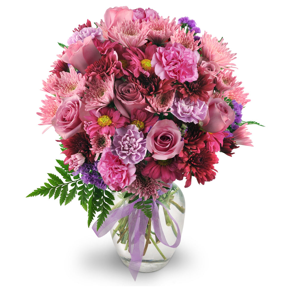 Purple Moon - Premium. Roses, carnations, chrysanthemums, and statice in shades of pleasing purples are expertly arranged in a clear rose vase.