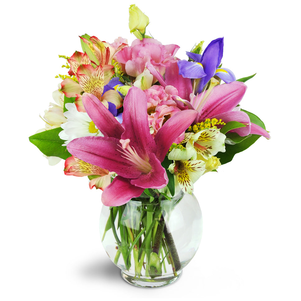 Sweet Symphony™ - Deluxe. Mauve lilies, blue iris, pink lisianthus, and more are arranged in a fluted bubble bowl.