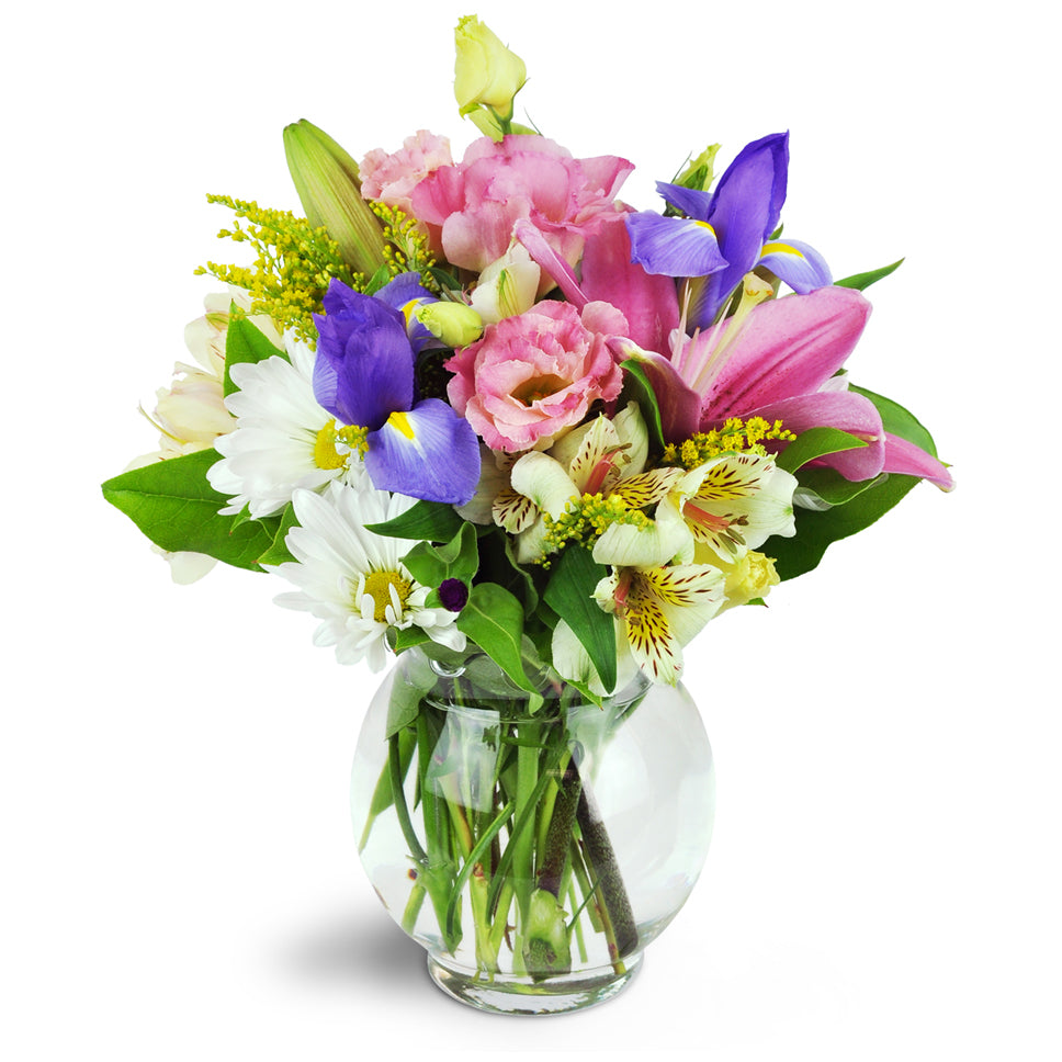 Sweet Symphony™ - Standard. Mauve lilies, blue iris, pink lisianthus, and more are arranged in a fluted bubble bowl.