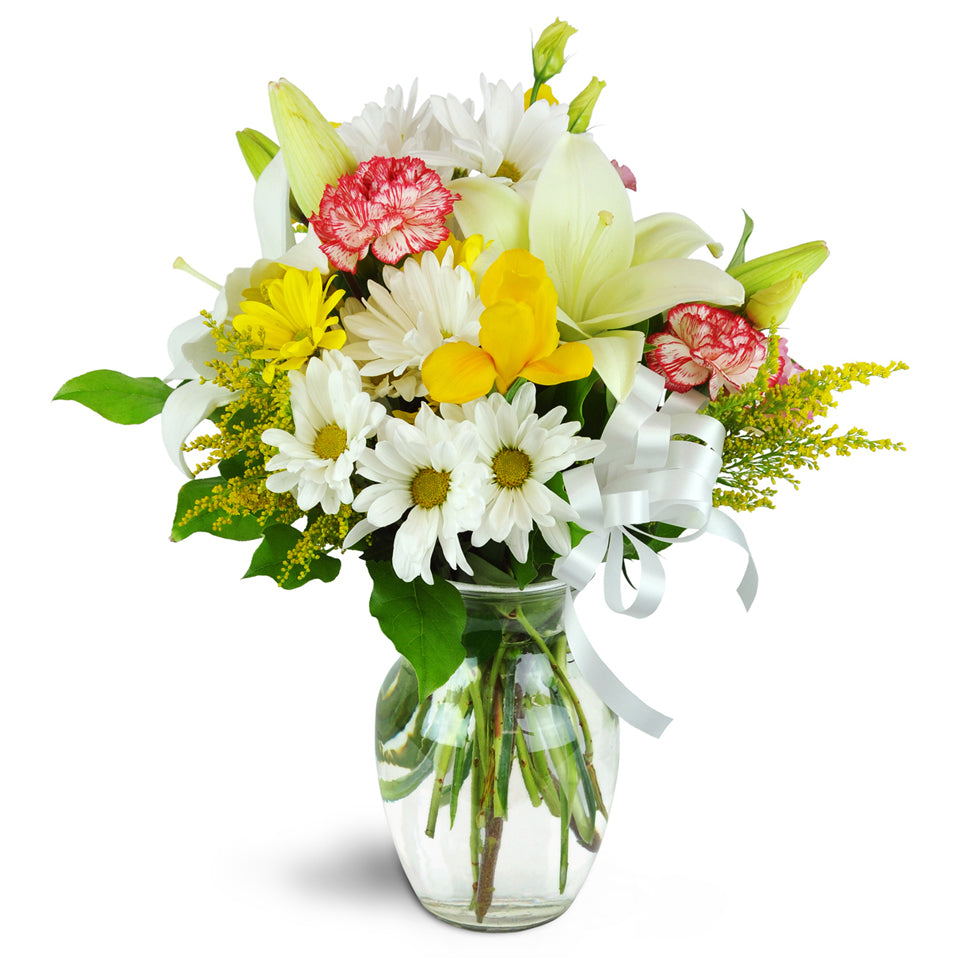 Pure Gladness™. Creamy lilies, cheerful yellow irises, white daisies, and more are arranged in a classic rose vase.