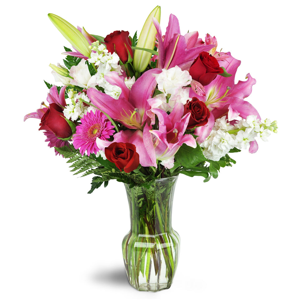 Blushing Heart Bouquet - deluxe flower arrangement. Deep red roses, lush lilies, and pretty pink Gerbera daisies are arranged in a clear glass vase.