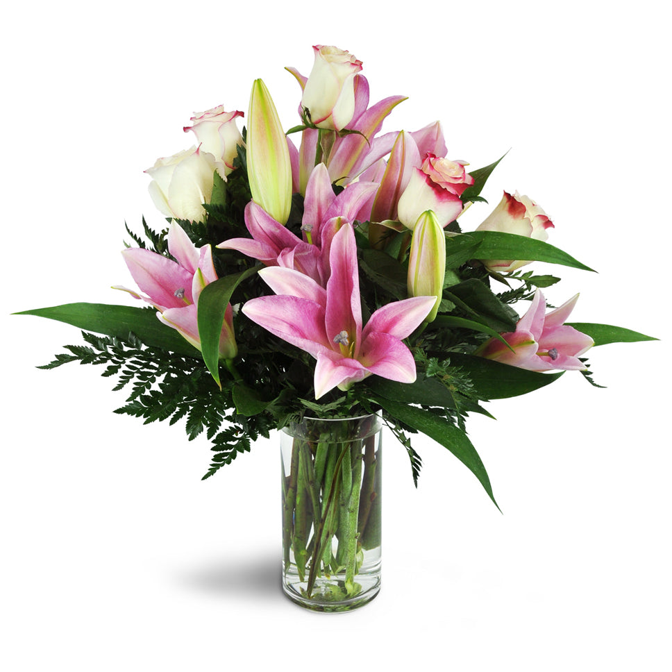 A sweet assortment of pink lilies and roses are arranged in a glass cylinder vase. Alluring Roses and Lilies flower arrangement.