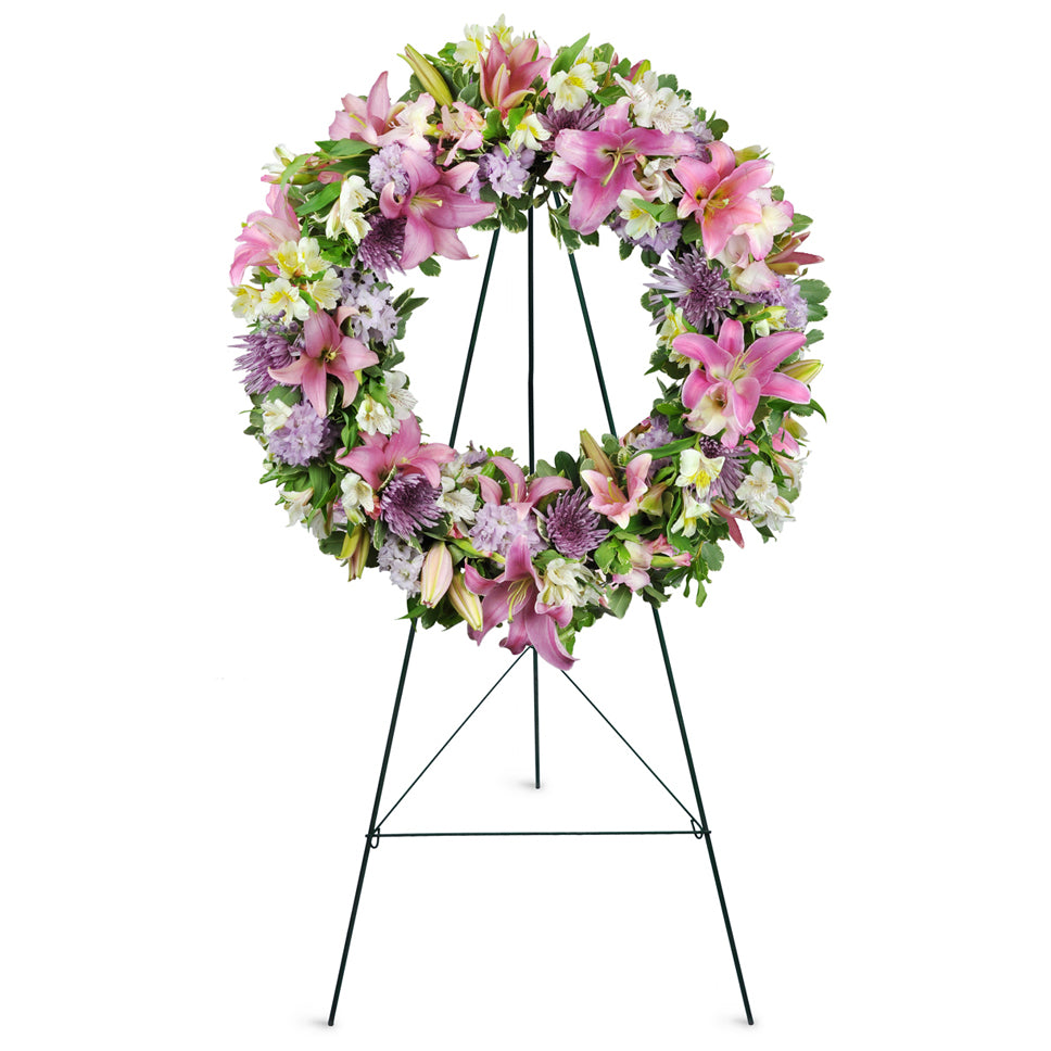 Encircled By Love™. Lilies, mums, larkspur, and more are gracefully arranged for display at the funeral home or service.