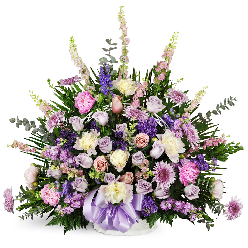 Love's Twilight Sympathy Basket™ - Premium. Larkspur, mums, and peonies are arranged with seasonal greenery and topped off with a satiny purple bow.